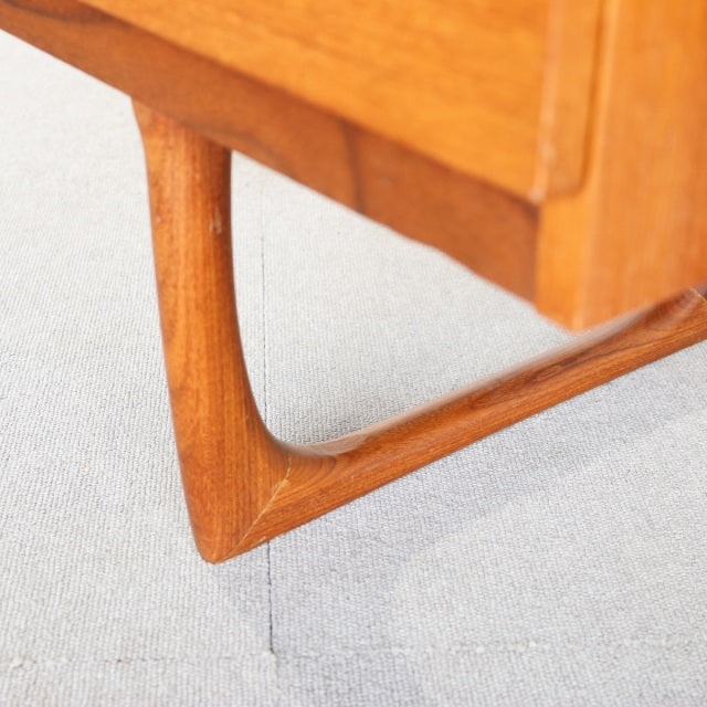 Close-up of vintage mid-century teak dresser leg with smooth, curved British design from Denmark, showcasing rich wood grain .
