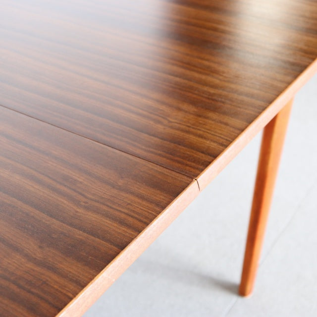 Vintage mid-century teak dining table with warm wood grain, rounded corners, and slender tapered legs, British-Danish design.