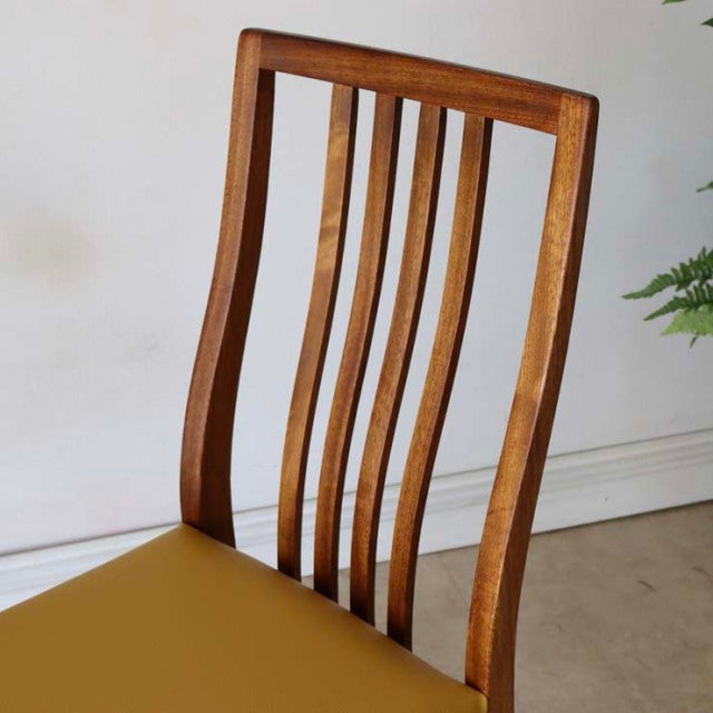 Mid-century British vintage teak dining chair with curved slat back and yellow seat cushion, smooth wood grain highlights.