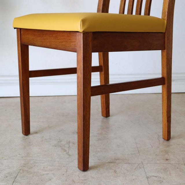 Vintage British mid-century teak dining chair with yellow seat and visible wood grain legs.