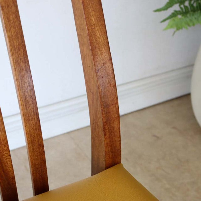 Mid-century British vintage teak dining chair backrest with rich wood grain and smooth finish, yellow seat partially visible.