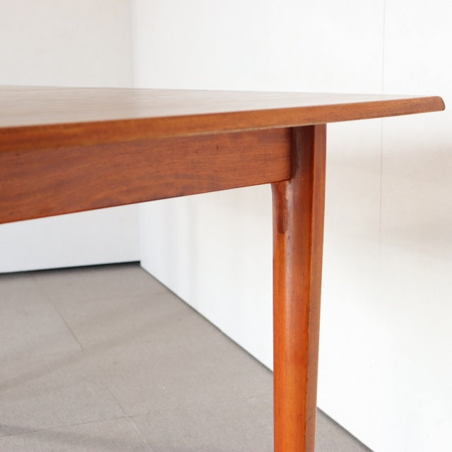 Vintage mid-century teak dining table corner with smooth wood grain and rounded British-Denmark style legs.