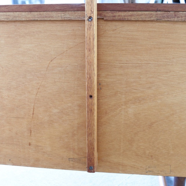 Vintage mid-century teak wood dresser panel with visible grain, supported by slender legs, British-Danish style.