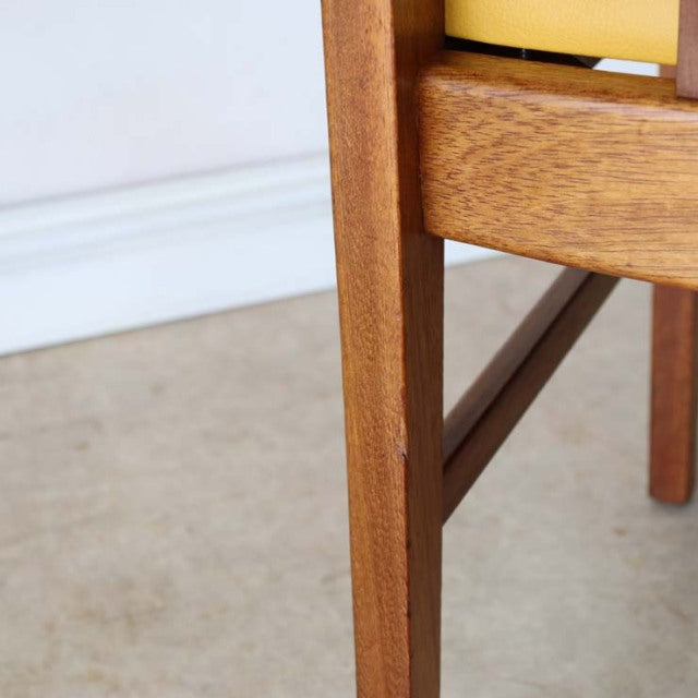 Close-up of vintage teak chair leg and frame showing warm wood grain and mid-century British craftsmanship with yellow seat.