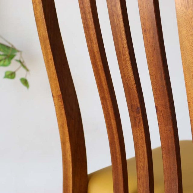 Mid-century British teak dining chair with yellow seat, sleek vertical slatted back, and gently curved wood grain legs in.