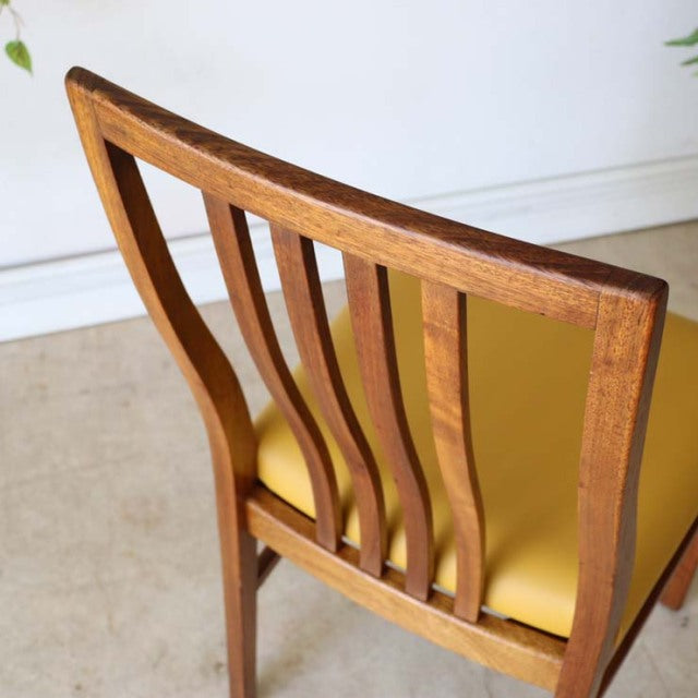 Mid-century British vintage teak dining chair with curved slat back and mustard yellow seat cushion.