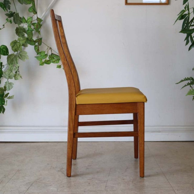 Mid-century British vintage teak dining chair with yellow seat cushion, sleek wood grain, straight legs, and simple elegant.