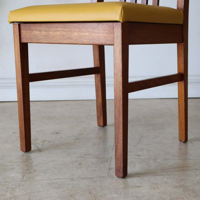 Mid-century British vintage teak dining chair with smooth wood grain and yellow upholstered seat, sturdy straight legs from.
