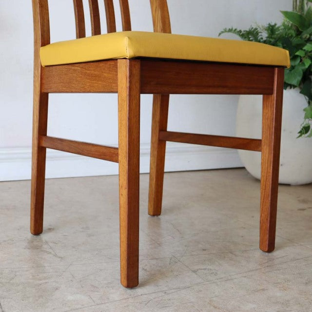 Mid-century British teak dining chair with yellow upholstered seat, straight tapered legs, and clean wood grain finish.