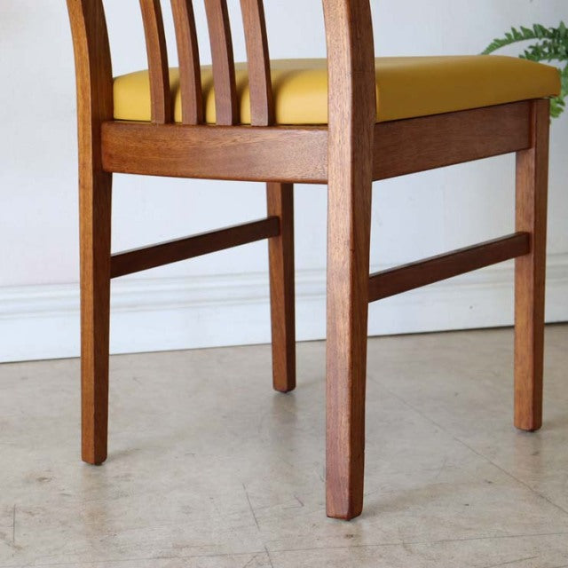 Mid-century British teak dining chair with yellow upholstered seat, vertical slat back, and sturdy square legs in vintage.