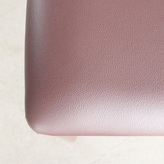 Close-up of vintage teak dining chair seat in smooth burgundy leather, showcasing fine grain texture and clean edges from.