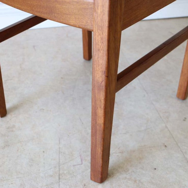 Mid-century teak dining chair leg detail with warm wood grain and brass-capped feet in vintage British-Danish style.