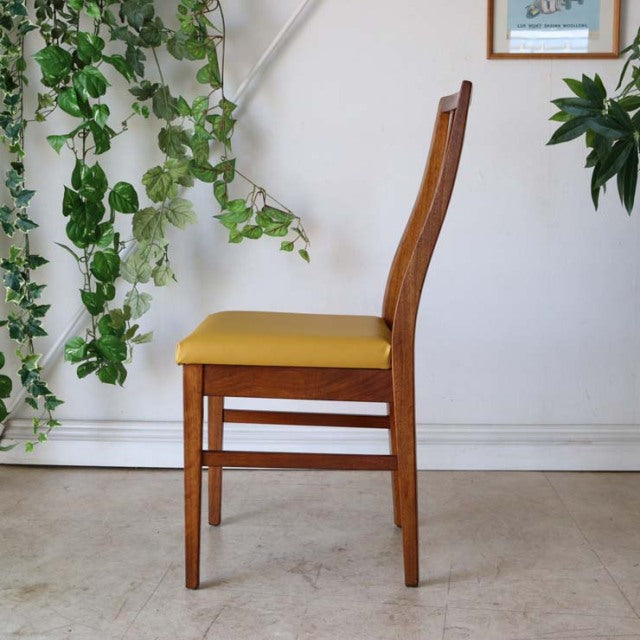 Mid-century British teak dining chair with curved backrest and vibrant yellow seat cushion in vintage condition.