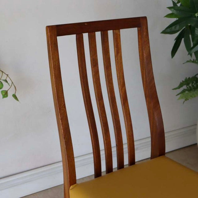 Mid-century British teak dining chair with yellow seat, slim vertical slats, and elegant curved backrest in vintage condition.