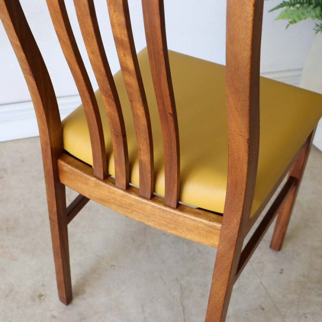 Vintage mid-century teak dining chair with yellow seat cushion, British design, curved slat back, slender tapered legs.