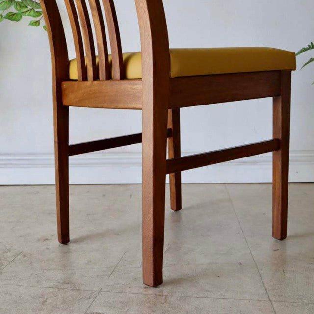 Vintage mid-century British teak dining chair with rich wood grain, vertical slatted back, and mustard yellow upholstered.