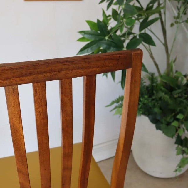 Vintage teak dining chair with yellow upholstered seat, British mid-century style, straight slatted backrest, smooth wood.