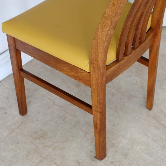 Set of four vintage mid-century teak dining chairs with mustard yellow seats, curved wooden backrests, and clean, sturdy.