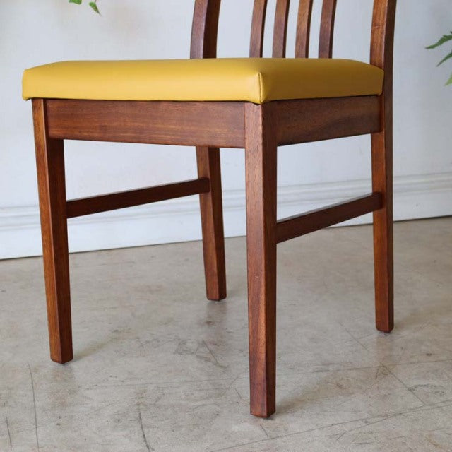 Vintage mid-century teak dining chair with yellow cushioned seat, sleek wooden legs, and curved British-Danish design.