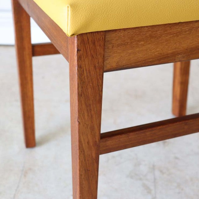 Mid-century British teak dining chair with yellow upholstered seat, visible wood grain, and sturdy square legs.