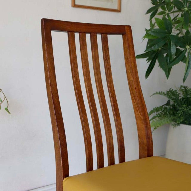 Mid-century vintage British teak dining chair with curved slat back and bright yellow seat cushion.