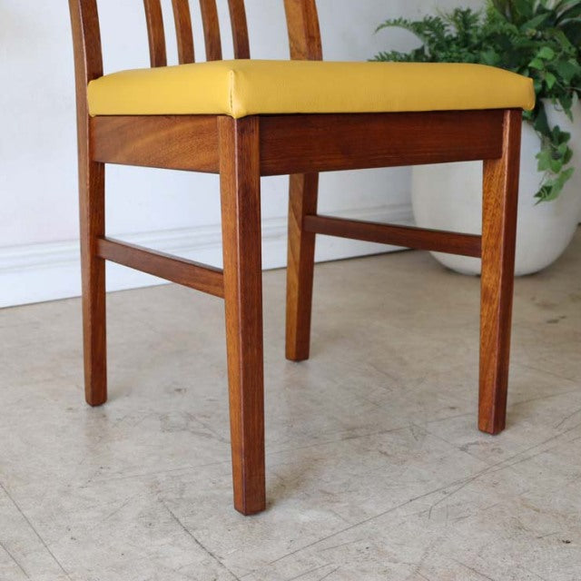 Mid-century British teak dining chair with yellow upholstered seat and clean wood grain legs.
