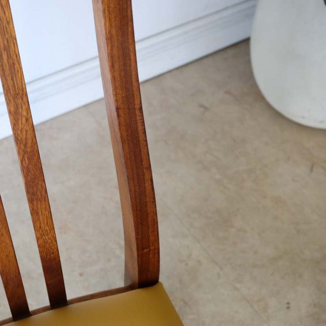 Mid-century British vintage teak dining chair leg with rich wood grain and yellow seat upholstery.