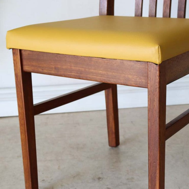 Mid-century British vintage teak dining chair with yellow upholstered seat and slatted backrest, showcasing rich wood grain.