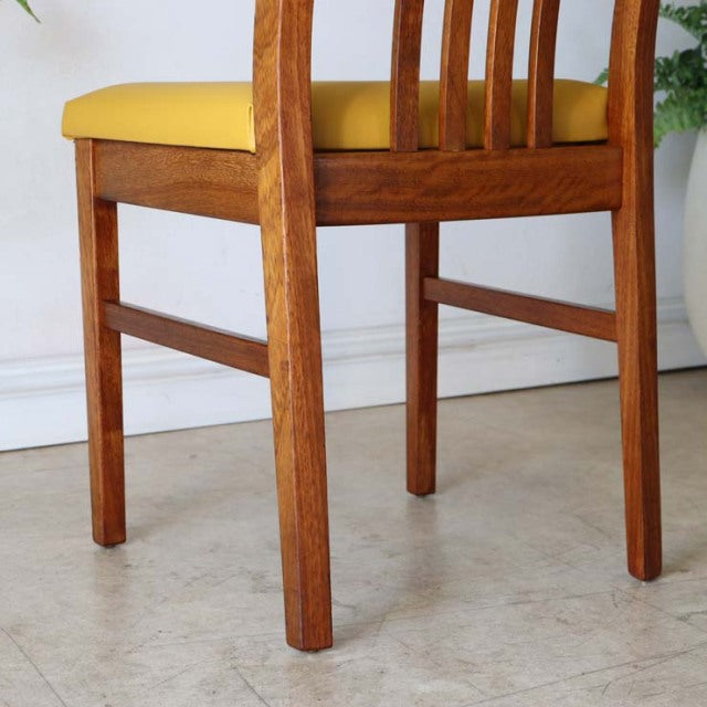 Mid-century teak dining chair with yellow seat cushion, British vintage style, Danish-inspired wood grain and slatted.