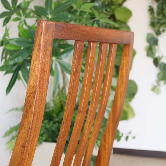Vintage teak dining chair back with slender vertical slats, warm wood grain, and mid-century British design.