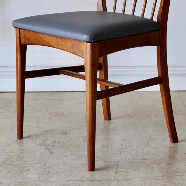 Vintage British mid-century teak dining chair with sharp backrest, black cushioned seat, and elegantly tapered legs.