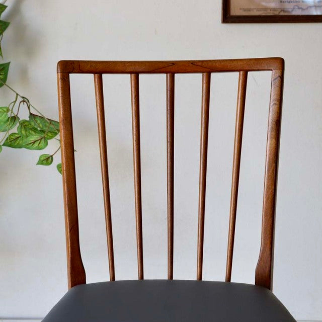Vintage teak dining chair with slim tapered back slats, mid-century British design, smooth wood grain finish.