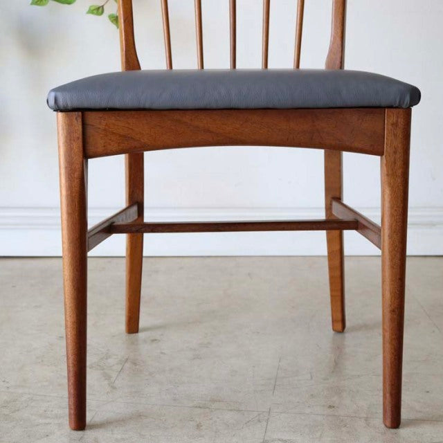 Vintage mid-century British teak dining chair with slender tapered legs, visible wood grain, and a dark upholstered seat.