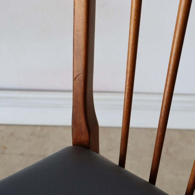 Vintage mid-century British teak dining chair with sharp backrest, slender vertical spindles, and black cushioned seat.