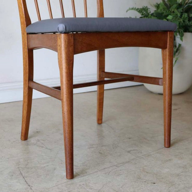 Mid-century British teak dining chair with sharp backrest, clean wood grain, and dark upholstered seat.