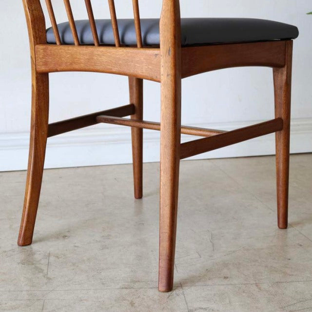 Mid-century vintage British teak dining chair with sharp backrest, spindle design, and black leather seat cushion.