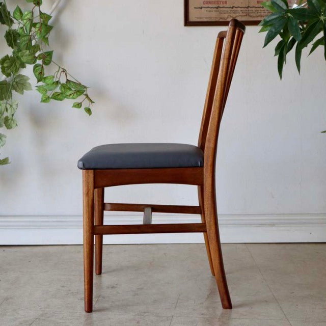 Vintage mid-century teak dining chair with sharply angled backrest, slender legs, and black cushioned seat, British-Danish.