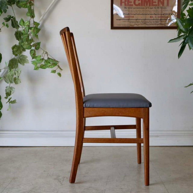 Mid-century British vintage teak dining chair with sharp backrest and gray upholstered seat, showing smooth wood grain and.
