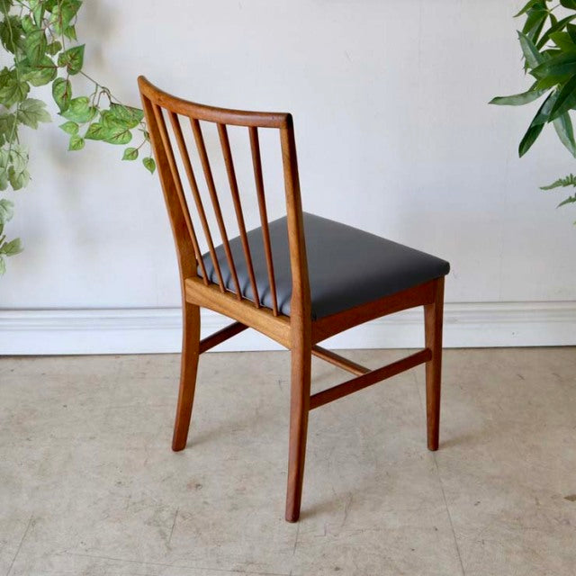 Vintage mid-century British teak dining chair with sharp backrest, slender vertical spindles, black upholstered seat, and.