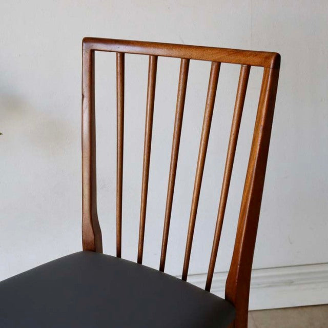 Vintage British mid-century teak dining chair with sharp backrest and vertical spindles, black seat cushion, slender tapered .