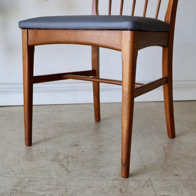 Mid-century British teak dining chair with sharp backrest, black upholstered seat, and visible wood grain detailing.