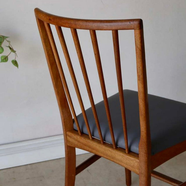 Vintage mid-century British teak dining chair with slender vertical spindle back and black cushioned seat.