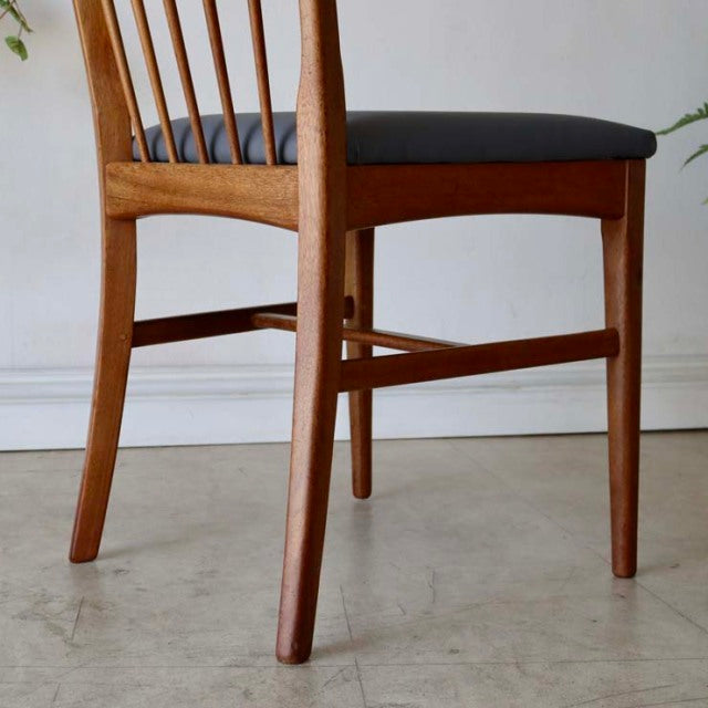 Vintage mid-century teak dining chair with slender tapered legs, sharp back spindles, and black upholstered seat,.