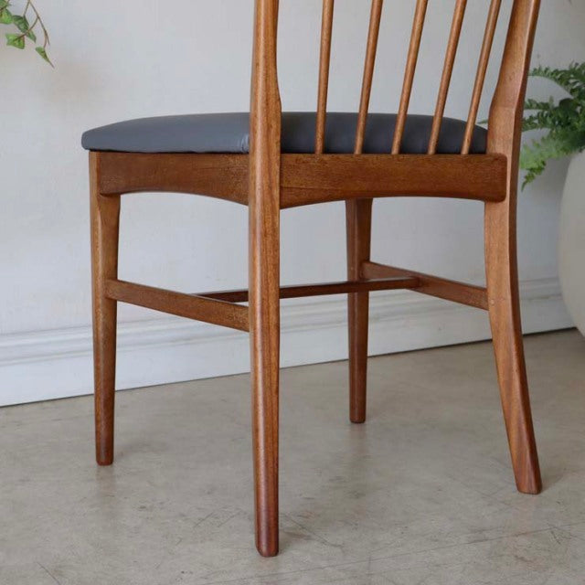 Vintage mid-century teak dining chair with slender spindled backrest, tapered legs, and black upholstered seat from.