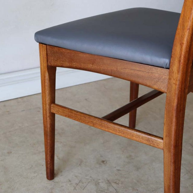 Vintage mid-century teak dining chair with smooth wood grain, tapered legs, and dark upholstered seat from British Denmark.