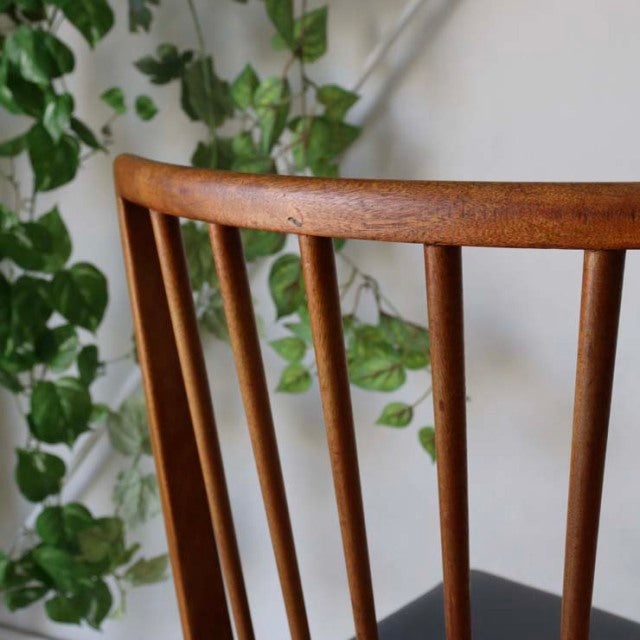Vintage teak mid-century British dining chair back with slender vertical spindles and smooth curved top rail against green.