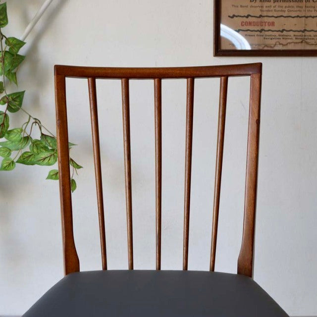 Vintage mid-century British teak dining chair with vertical spindle back and black upholstered seat.
