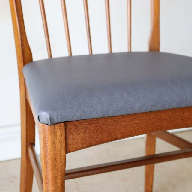 Vintage mid-century British teak dining chair with sharp backrest, smooth dark gray cushion, slender vertical slats, and.