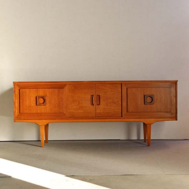 Mid-century British vintage teak sideboard with smooth wood grain, rounded recessed handles, and tapered legs.