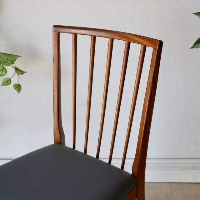 Vintage mid-century British teak dining chair with slender vertical spindle back and smooth black leather seat cushion.